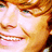 Pixelated close-up of a smiling person with light brown hair, visible teeth, and warm-toned skin under soft lighting.