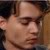 Pixelated close-up of a person's face with closed eyes, showing partial ear and neck, against a blurred background with brown and dark tones.