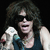 Pixelated image of a person with long dark hair holding a white dog, wearing a dark sleeveless top against a black background.