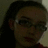 Pixelated close-up of a person with dark hair and glasses, wearing a dark top against a muted background.