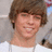 A pixelated close-up of a person with brown hair wearing a white shirt, smiling against a light background.