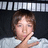 Pixelated image of a person with short brown hair resting their chin on a hand, wearing a light-colored shirt against a dark background with horizontal light stripes.