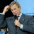 Pixelated image of a man in dark suit adjusting tie with hand on head, next to blue pixelated text blocks.