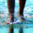 Pixelated image showing two figures' legs and feet standing on a light blue background with white cloud-like shapes.
