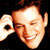 Pixelated static icon of a smiling man's face with visible facial features and partial text on the left side against dark background.