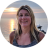 Pixelated circular portrait of a person with long light brown hair wearing a dark top with blue accents, set against a sunset sky with orange and blue hues.