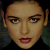 Pixelated close-up of a person's face with light skin, dark eyebrows, and red lips against a dark background.
