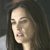 Pixelated close-up of a person with long dark hair, light skin, and closed eyes, wearing a dark top against a dark background.