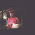 Pixelated figure in red top and dark pants holding a white object against dark background