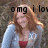A person with long red hair wearing a light blue cardigan over a red top, standing outdoors against a blurred background.