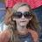Pixelated image of a person with light brown hair wearing dark sunglasses and a red headband, set against a blue background.