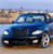 Blue sedan with headlights on, positioned on a road with blurred background, viewed from front-left angle.