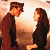 Two pixelated figures face each other against a warm-toned gradient background, one in dark clothing with a cap, the other with long dark hair.