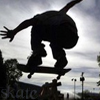 Silhouette of a person performing a skateboarding trick against a cloudy sky background with visible urban elements.