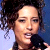 Pixelated close-up of a person with dark curly hair against a blue and light blue gradient background, mouth slightly open.