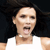 Pixelated close-up of a person with dark hair wearing a white shirt against a dark background, mouth open in a shout or yell.