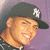 Pixelated image of a person wearing a dark cap with white emblem, light brown hair, and smiling expression against purple background.