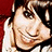 Pixelated close-up of a smiling person with light skin, dark hair, and visible eye details against red and black background elements.
