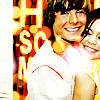 Two people in close proximity, one wearing a white shirt with red stripes, the other in a yellow patterned top, with large stylized text in the background.