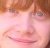 Pixelated close-up of a person's face with light brown hair, pinkish skin tones, and visible eyes and mouth.