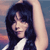 A pixelated static image shows a person with long dark hair wearing a white top against a blurred background with blue and pink tones.
