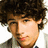 Pixelated image of a person with curly brown hair wearing a light-colored jacket over a white shirt, with pink text elements surrounding the figure.