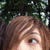 A pixelated close-up of a person's face with light brown hair and one visible eye, set against dark green foliage.