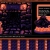 Pixelated static image showing a dark interior with a computer monitor displaying a grid of small squares and a figure in orange and purple tones.