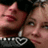 Two people in close proximity, one wearing a black top with a white and black patterned design, the other with light-colored hair and a neutral expression.