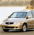 A light-colored sedan with a dark roof is positioned at a slight angle, viewed from the front-left side against a blurred background of sky and ground.