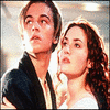 Static image of two people in close proximity, one with dark hair and dark clothing, the other with long brown hair and light clothing, both looking upward.