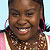 Pixelated image of a smiling person with dark skin, short dark hair, and a patterned top with pink and brown tones.
