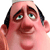 Pixelated cartoon-style face with pinkish skin, dark hair, green eyes, and a slightly open mouth showing teeth.