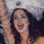 A pixelated close-up of a person with long dark hair, mouth open in a shout or laugh, against a blurred background with light and dark tones.