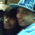 Two people in close proximity, one wearing a blue patterned cap and dark clothing against a light background.