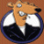 Static pixelated icon of a cartoonish animal head with large white eyes and black nose inside a blue circular border on brown background.
