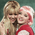 Two figures with light hair embrace; one wears a red top with white accents against a muted green background.