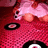 Pixelated image of a pink-clad figure on a red patterned surface with visible text reading "Music is Love" in pink letters.