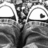 Black-and-white pixelated image of a stylized figure with outstretched arms, two large circular shapes on either side, and a dark vertical element below.
