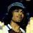 Pixelated image of a person with long dark hair wearing a blue cap and white shirt, set against a dark background.