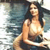 A pixelated image of a person with long dark hair wearing a dark bikini top, seated in a light-colored chair against a blurred background.