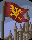 Pixelated flag with yellow emblem on maroon field, mounted on pole above castle silhouette against blue sky, show flag movement