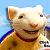 Pixelated cartoon pig character in yellow outfit with blue shoulder accents and red collar, smiling against light blue background.