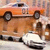 Static pixelated image of an orange vehicle with dark wheels and a white front section, positioned on a light background.