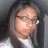 Pixelated static image of a person with long dark hair wearing glasses and a white collared shirt against a gray background.
