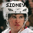 Pixelated image of a person wearing a white helmet with black text reading 'SIDNEY' above the head, set against a blurred background.