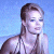Pixelated image of a person with light brown hair tied back, wearing a white halter top and multiple necklaces against a blue background.