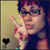 Pixelated image of a person with dark hair and glasses making a peace sign, wearing red lipstick and a dark top against a gradient background.