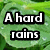 Green leaf background with water droplets and black-outlined white text reading "A hard rains" in top-left, "a gonna" in top-right, and "fall" in bottom-left.