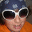 Pixelated close-up of a person wearing dark sunglasses with white frames, an orange garment, and a dark blue background with light speckles.